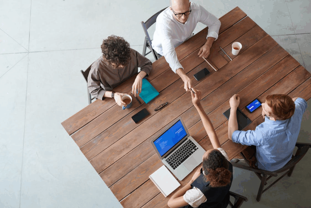 Overhead view of a small group of creatives meeting around a wooden table, building offline creative community.