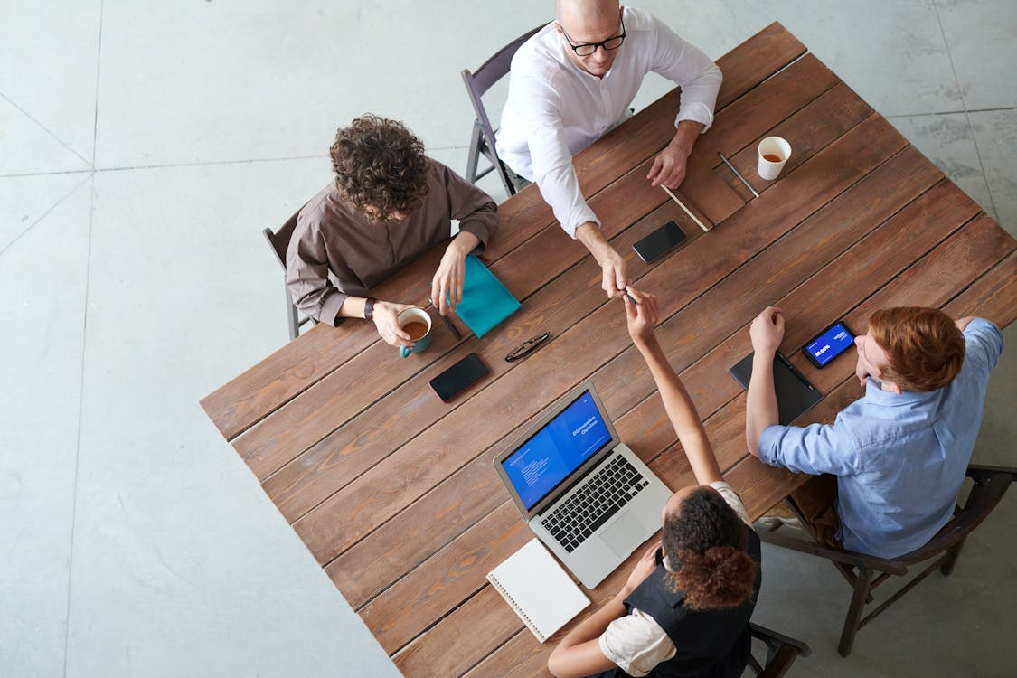 Overhead view of a small group of creatives meeting around a wooden table, building offline creative community.