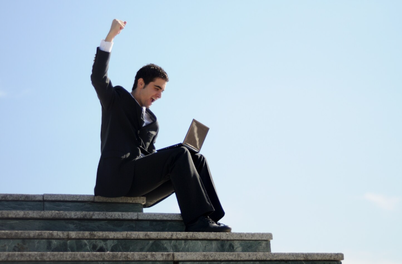 Young man in a suit celebrating while working on a laptop, symbolizing creative career success.