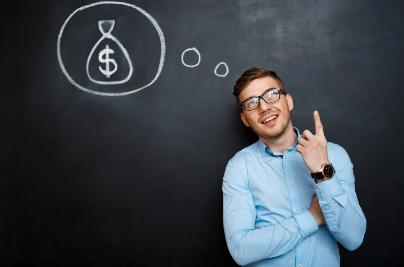Smiling creator standing by a chalkboard with a money bag doodle, rethinking their money mindset.