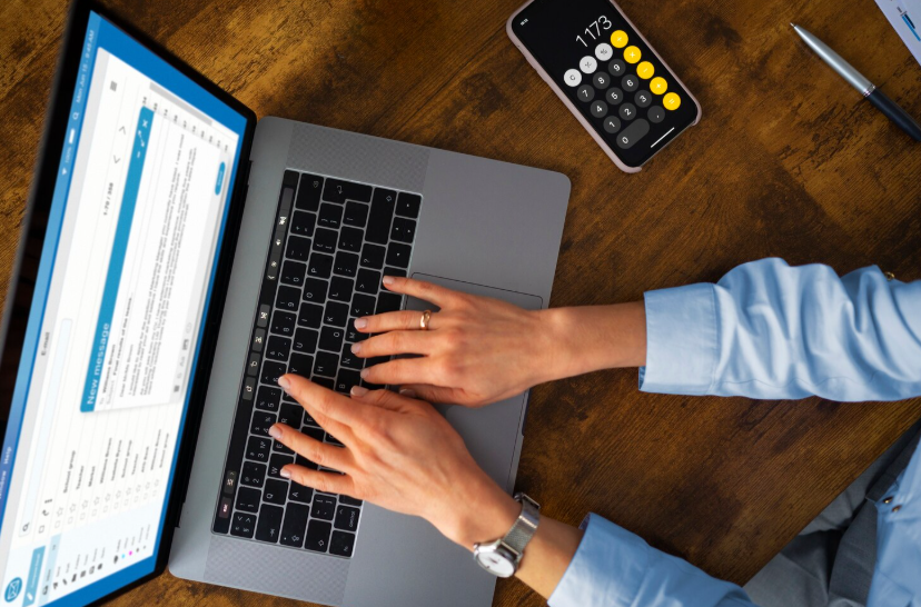 Overhead view of creator using a laptop and calculator to calculate fair pricing for creative work.