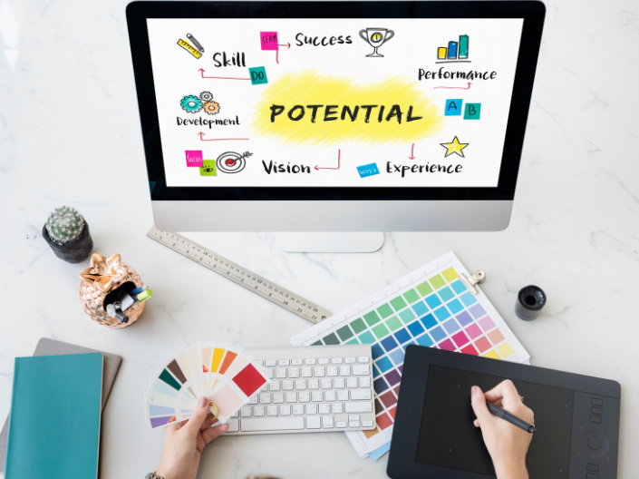 Overhead view of designer at desk with a screen showing the word “Potential” with icons for success, vision, and growth.