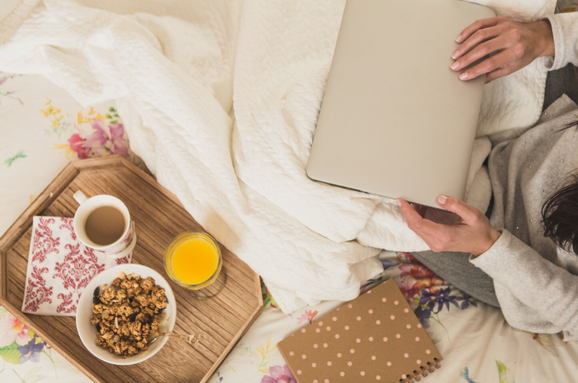 Overhead view of a creator working on a laptop in bed with coffee and a breakfast tray.